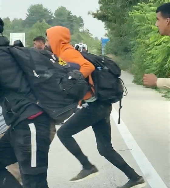 Περίπου 20 νεαροί άνδρες φορτωμένοι με σακίδια πλάτης τρέχουν μπροστά από τα ακινητοποιημένα αυτοκίνητα και χάνονται μέσα στα χωράφια.